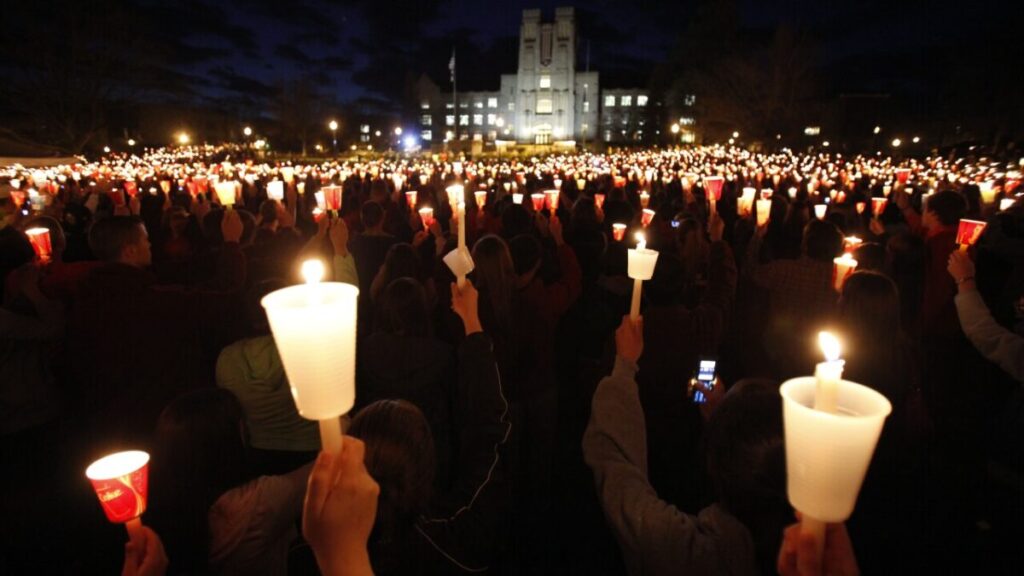 Participants holding lit candles during a candlelight vigil at night with a building in the background.