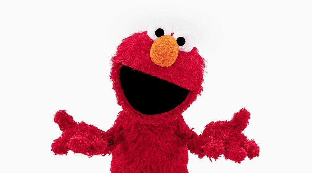 Elmo, a red furry character with a round orange nose and wide mouth, standing with arms outstretched.