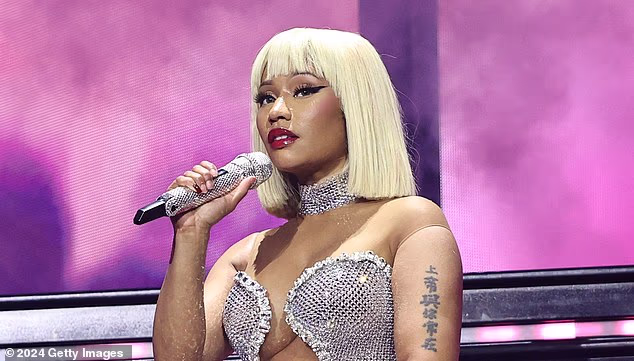 Nicki Minaj holding a microphone while performing on stage with a sparkly outfit and blonde bob hairstyle.