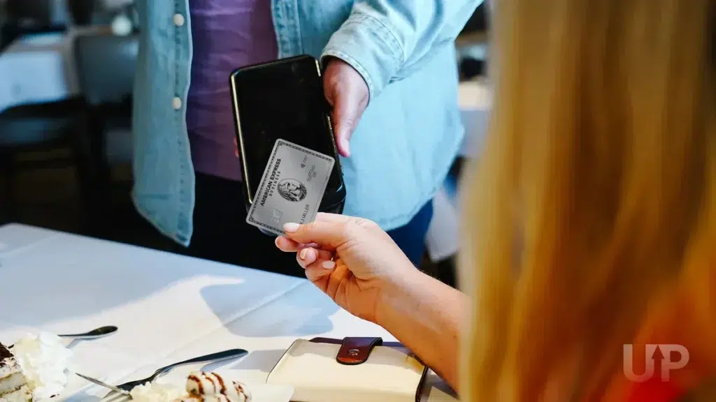 A person holding an American Express Business Platinum card while another person presents a tablet.