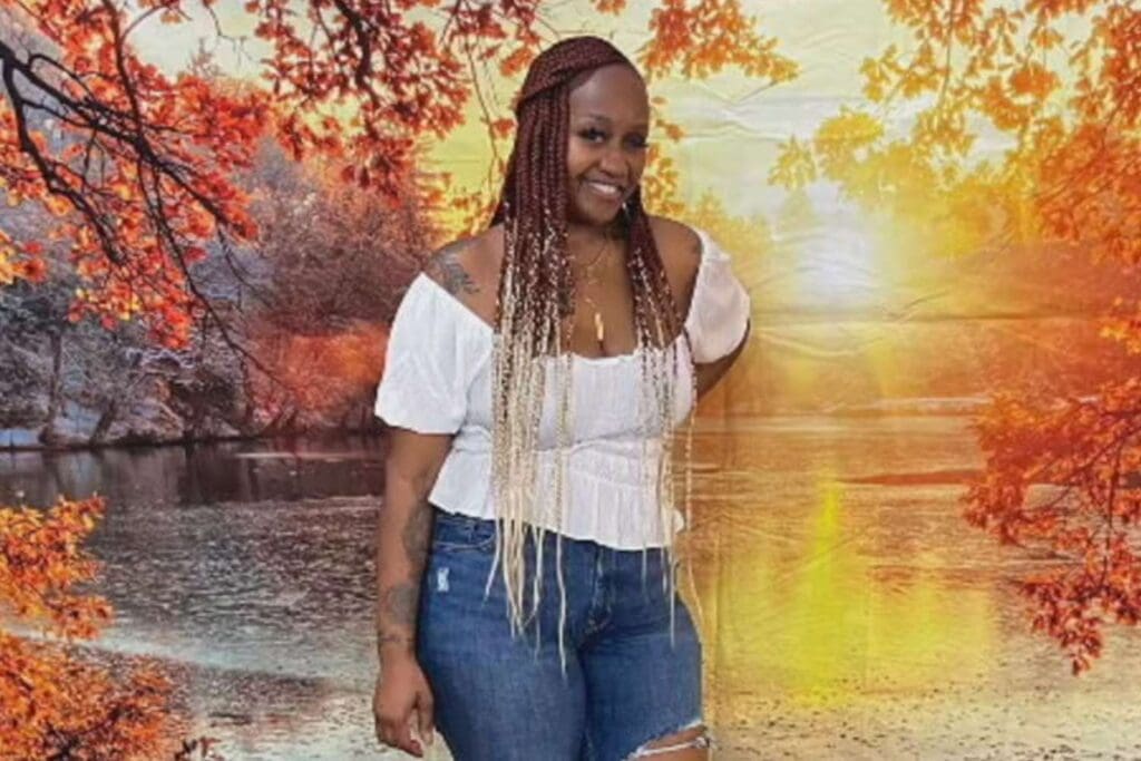 Woman with braided hair wearing a white top and jeans, posing in front of a nature backdrop.