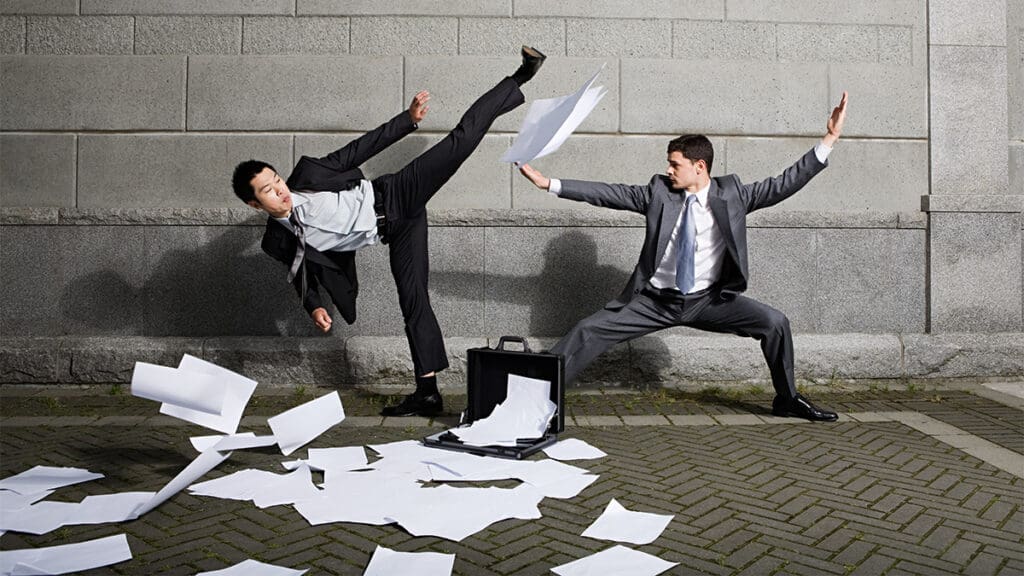 Two businessmen in suits in a physical altercation with papers scattered on the ground.