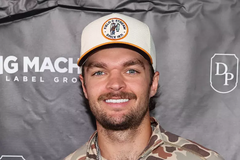 Conner Smith smiling while wearing a cap and a patterned shirt at an event.