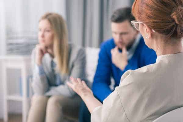 A couple sitting apart during a mediation session with a mediator gesturing while speaking.