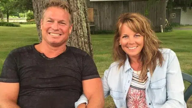 A man and a woman smiling while sitting outdoors near a tree.