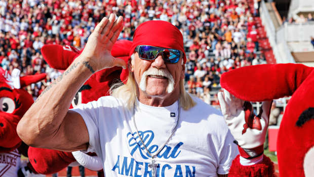 Hulk Hogan wearing sunglasses and a red bandana, saluting at a sports event.