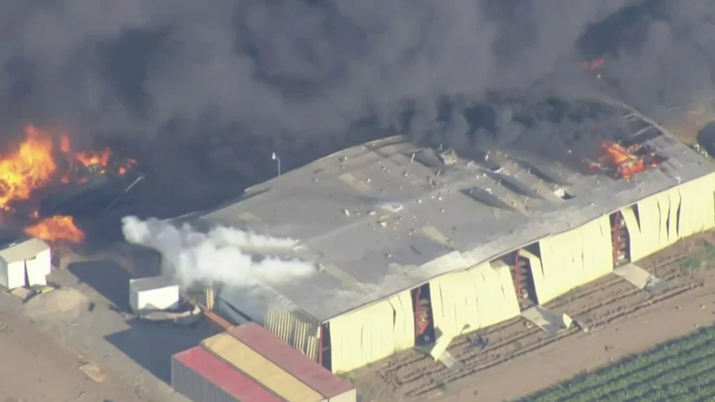 Aerial view of a warehouse engulfed in flames and smoke during a fire incident.