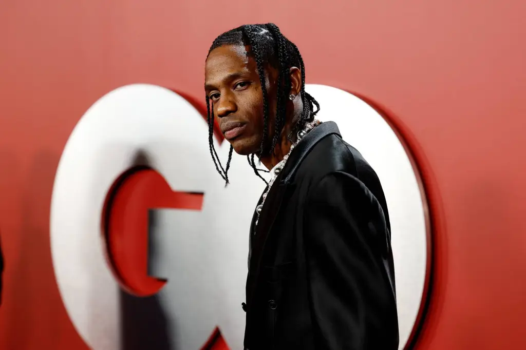 Travis Scott posing for a photo at a red carpet event with a logo in the background.